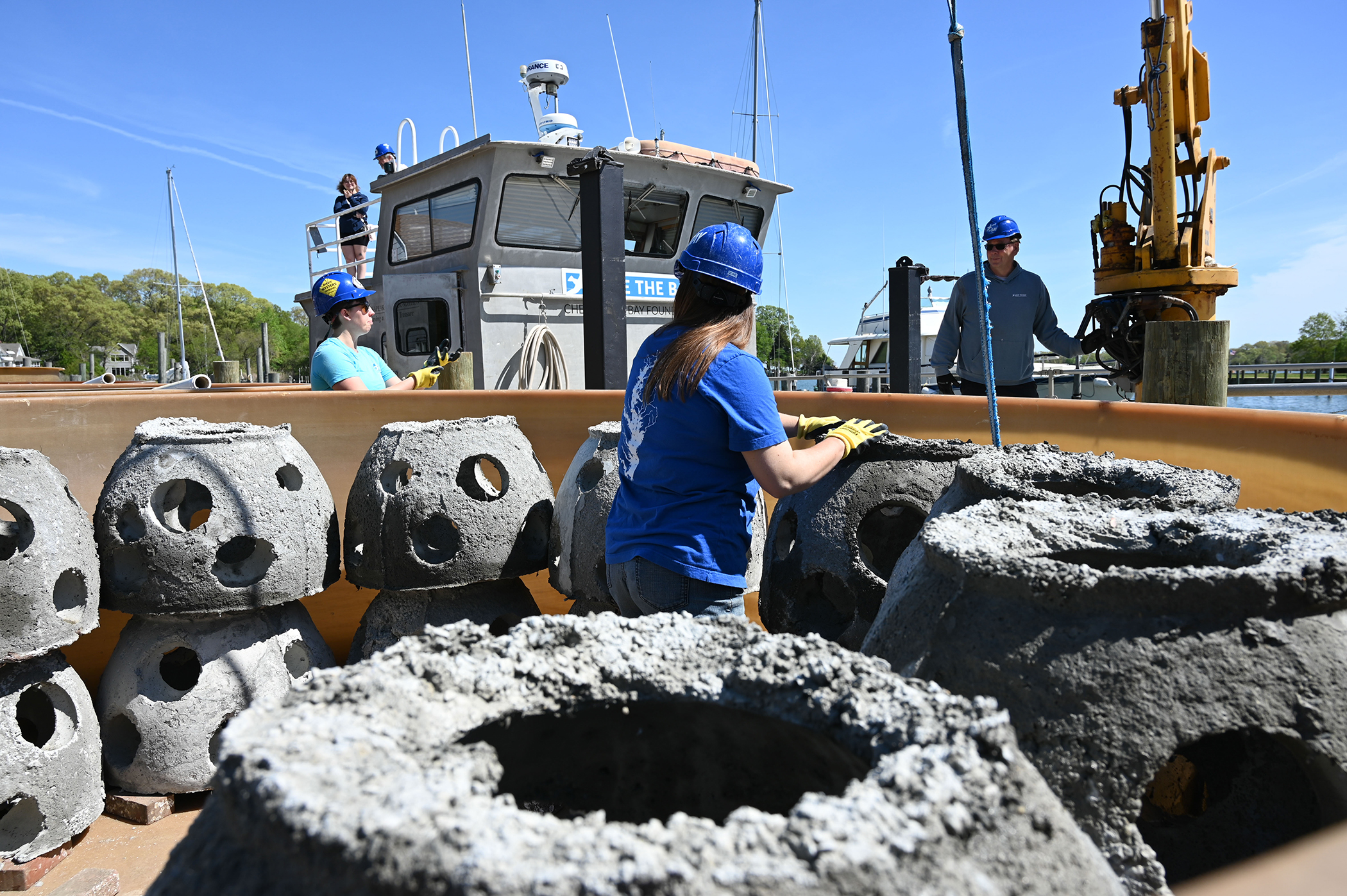 A woman places a reef ball into a 3,000-gallon tank with other reef balls. A man operating a crane stands by.